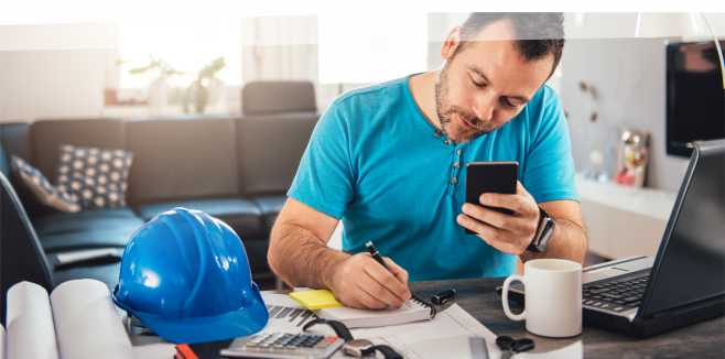 Productivity losses in projects. Justified claims due to work in home office, instructed by authorities. Source: istockphoto.com, Copyright: Kerkez, Picture Man in blue shirt writing notes and holding smart phone at home office